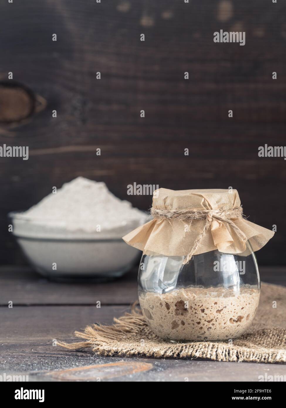Levain de seigle active du démarreur dans le bocal de verre et la farine de seigle sur fond de bois brun. Démarreur pour pain au levain. La tonalité de l'image. Copier l'espace. La verticale Banque D'Images
