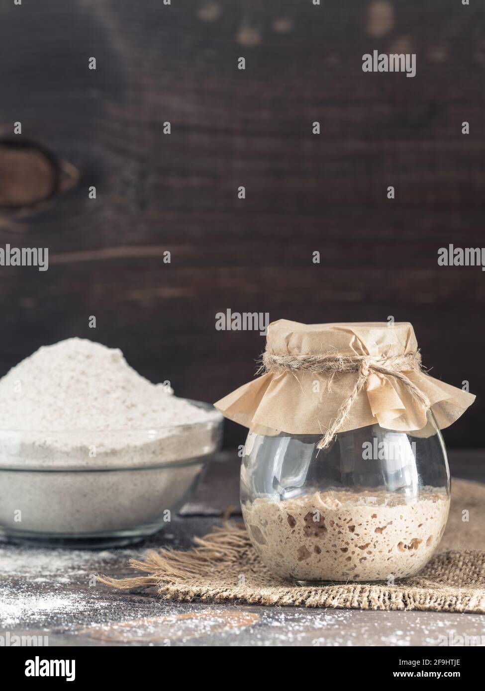 Levain de seigle active du démarreur dans le bocal de verre et la farine de seigle sur fond de bois brun. Démarreur pour pain au levain. La tonalité de l'image. Copier l'espace. La verticale Banque D'Images