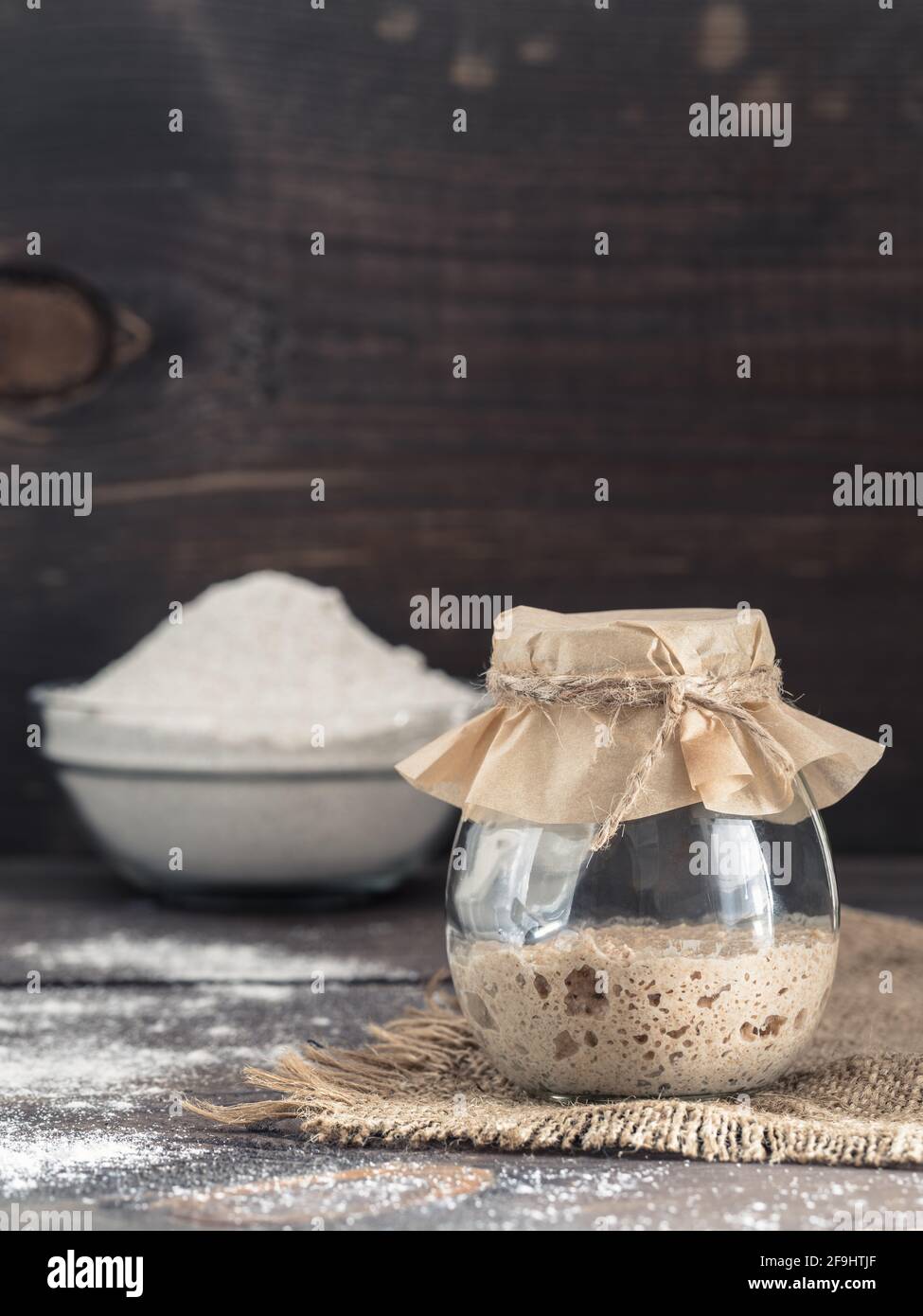 Levain de seigle active du démarreur dans le bocal de verre et la farine de seigle sur fond de bois brun. Démarreur pour pain au levain. La tonalité de l'image. Copier l'espace. La verticale Banque D'Images