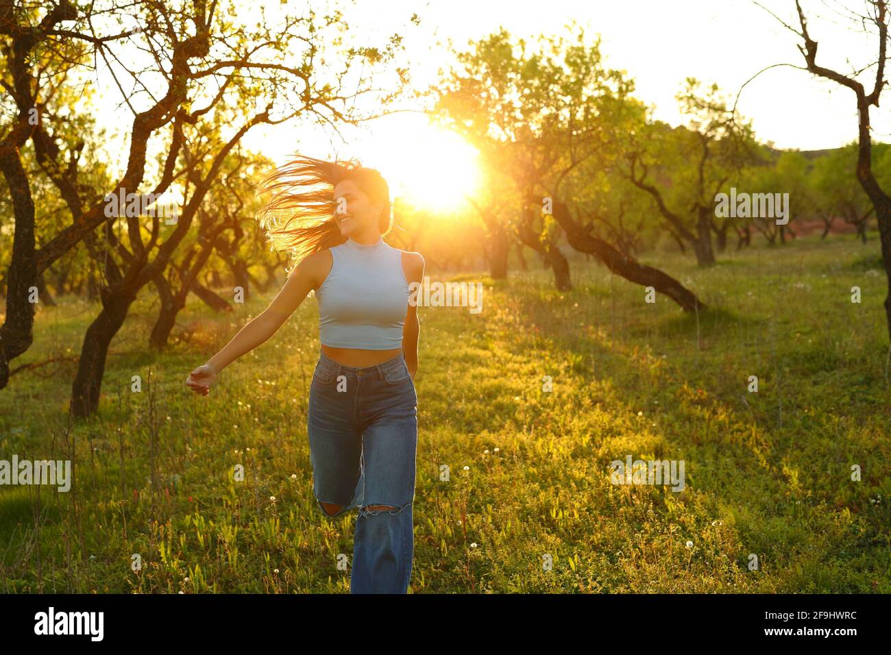 Vue avant d'une femme heureuse qui court vers l'appareil photo à coucher de soleil dans un champ Banque D'Images