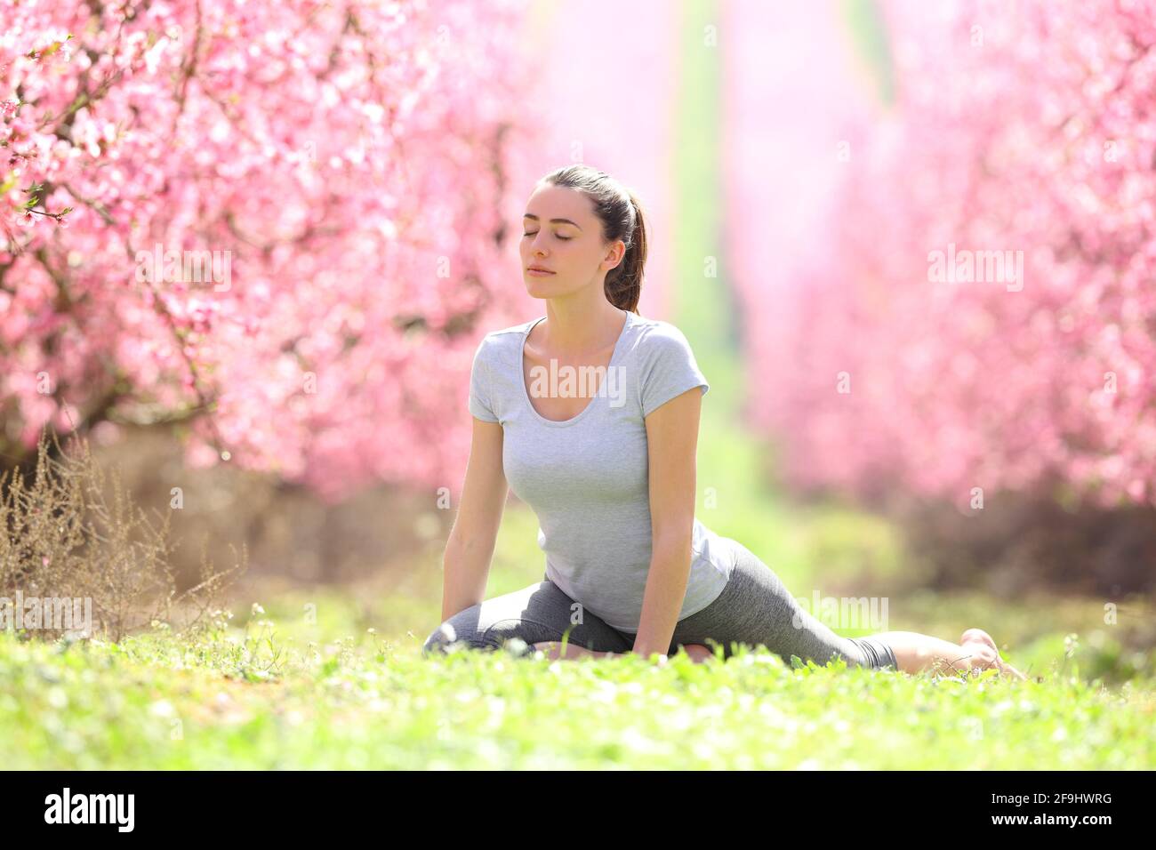 Femme concentrée pratiquant l'exercice de yoga sur l'herbe dans un champ fleuri au printemps Banque D'Images