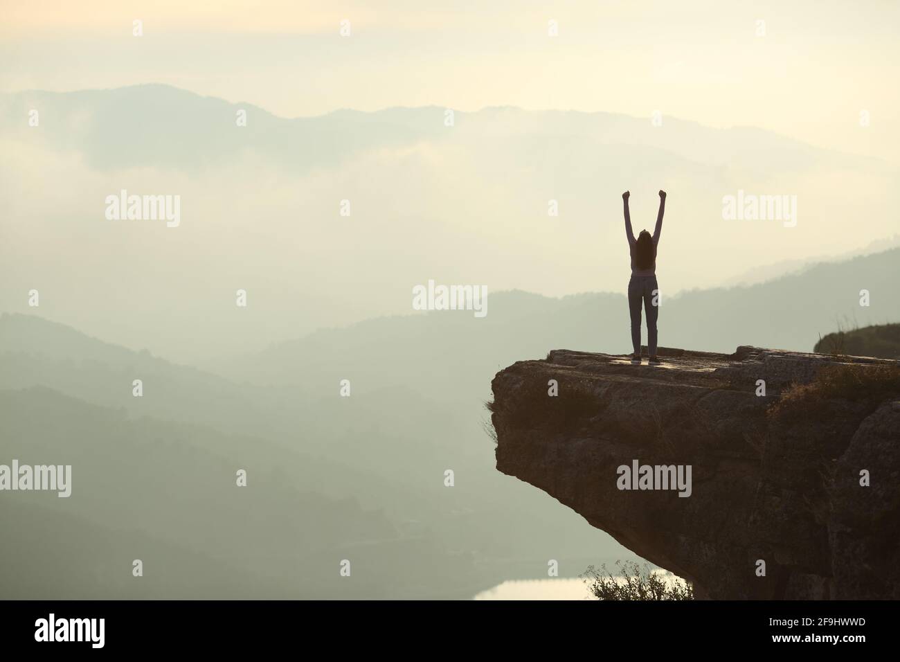 Vue arrière portrait d'une silhouette de femme célébrant le soulèvement des bras en haut d'une falaise dans la montagne Banque D'Images