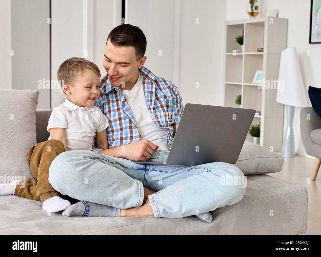 Un jeune père heureux et un petit fils mignon utilisant un ordinateur portable à la maison. Banque D'Images