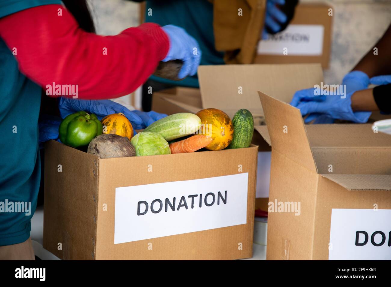 Groupe de bénévoles méconnaissables qui travaillent en organisant des légumes et des vêtements sur des boîtes de dons pendant le confinement de la pandémie de covid-19 du coronavirus Banque D'Images