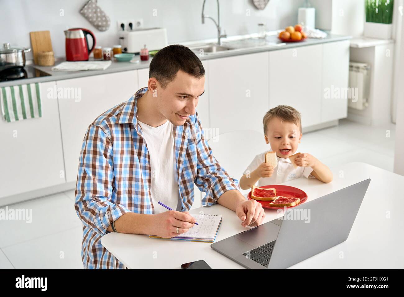 Père travaillant à domicile avec un ordinateur portable assis à une table avec un enfant mignon fils. Banque D'Images