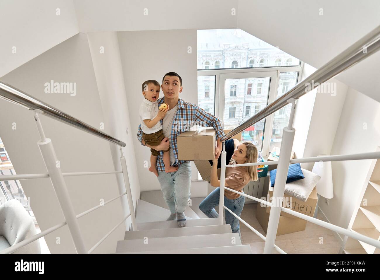 Une famille heureuse avec des boîtes de transport pour fils d'enfants à l'étage arrivant dans une nouvelle maison. Banque D'Images