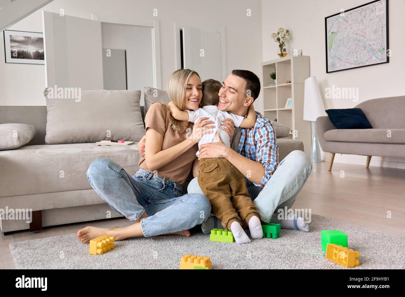 Joyeux jeune couple de famille embrassant mignon petit garçon d'enfant assis sur le sol à la maison. Banque D'Images