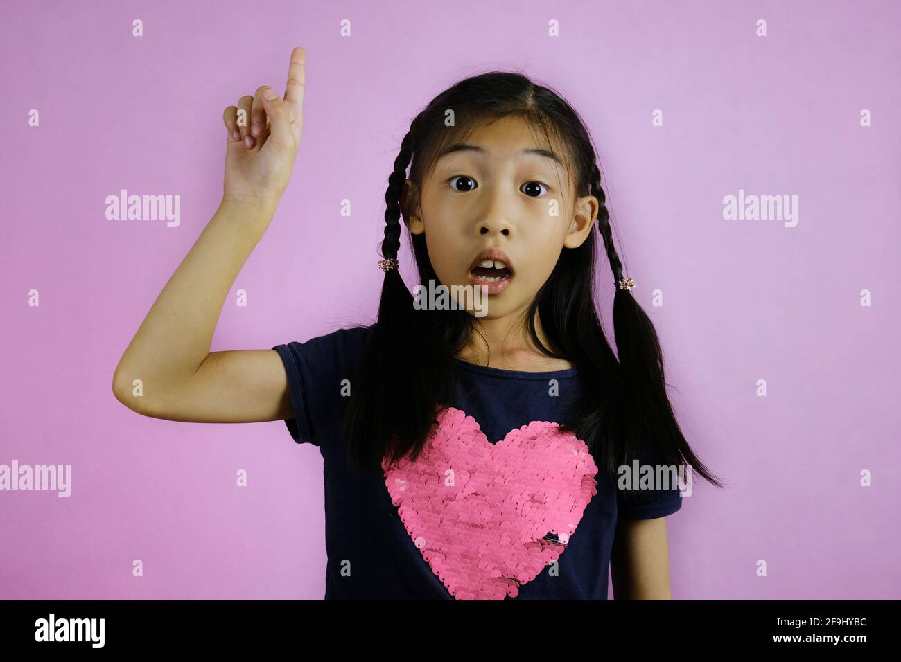 Une jeune fille asiatique mignonne gestuelle qu'elle a une idée en pointant son doigt vers le haut avec un visage confiant. Fond rose vif. Banque D'Images