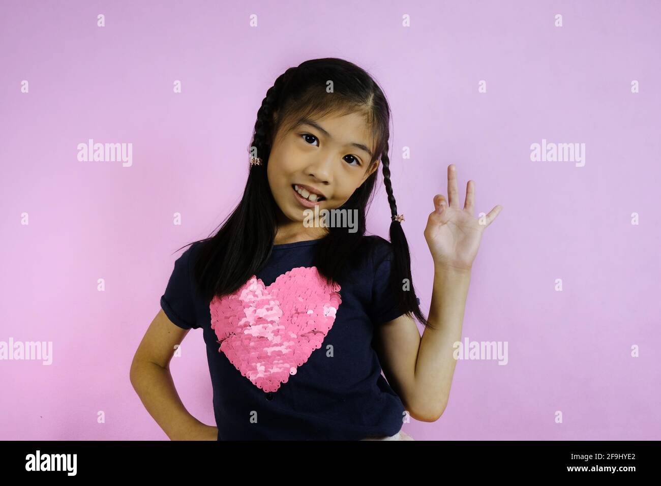 Un demi-coup de corps d'une jeune fille asiatique mignonne, tenant sa main gauche, en signe ok, se sentant confiant dans sa mission. Banque D'Images