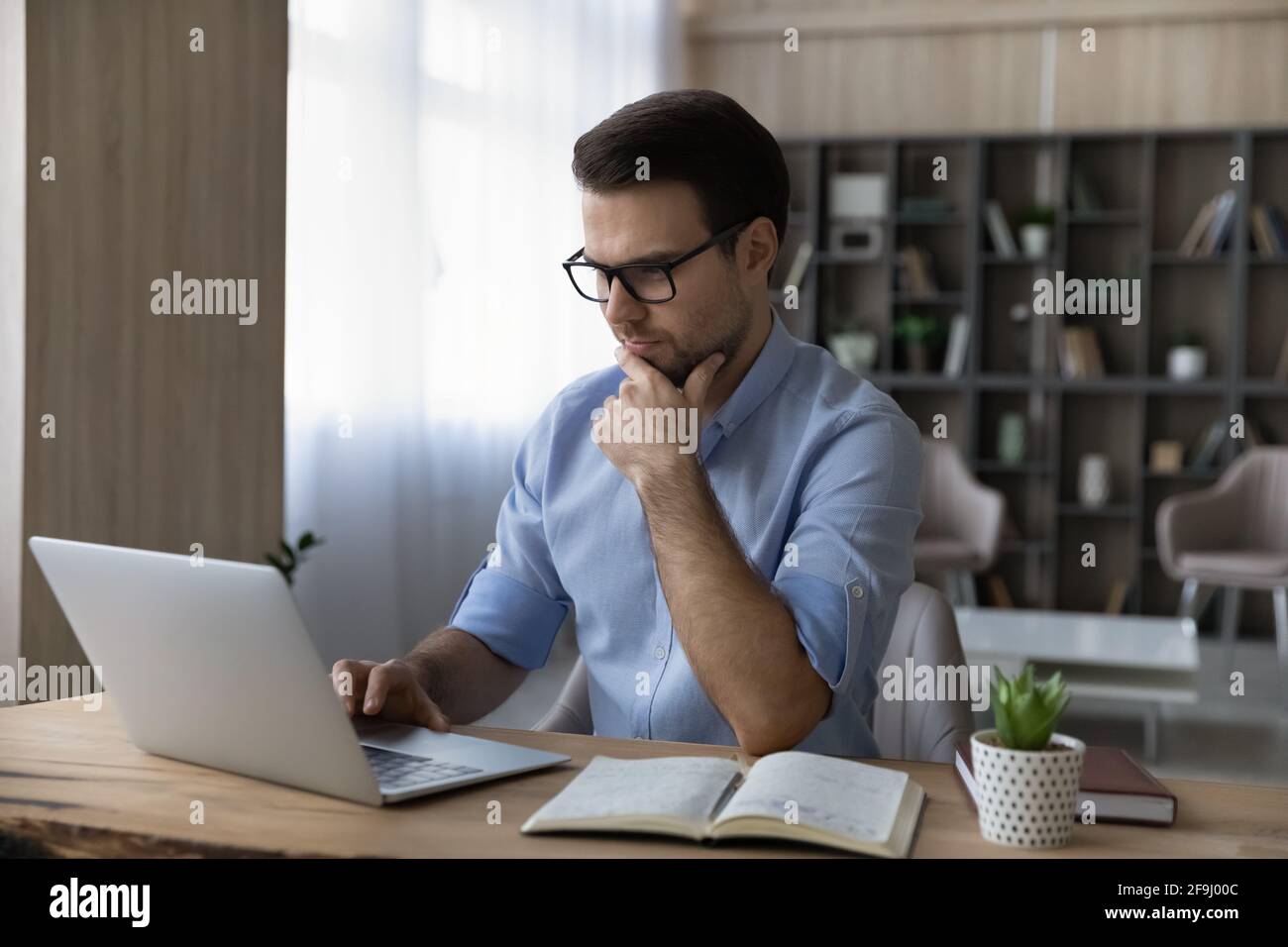 Un homme pensif travaille sur un ordinateur portable pour prendre des notes Banque D'Images