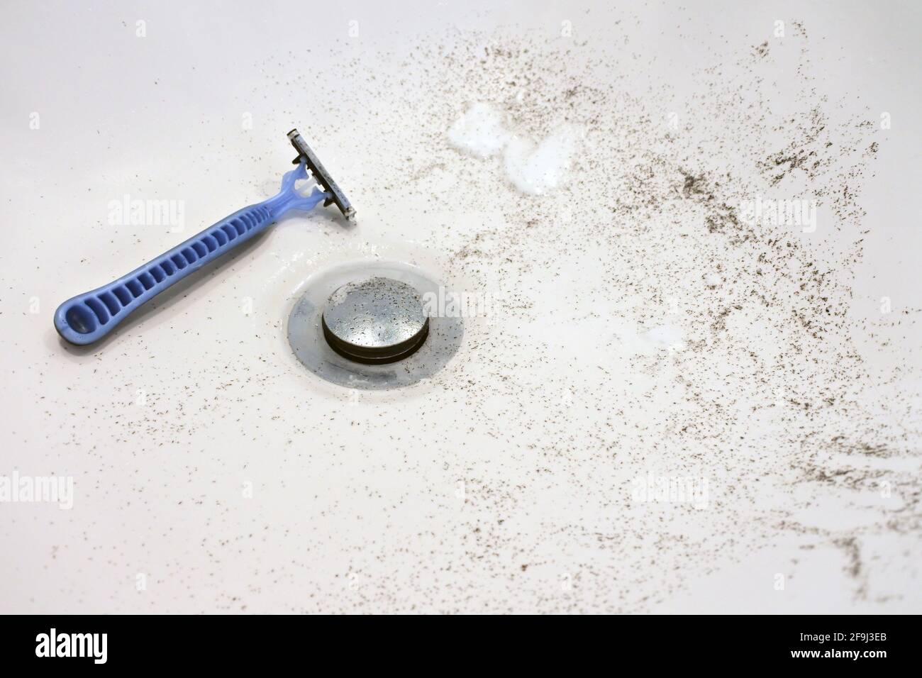 Rasoir avec poils rasés dans un lavabo de salle de bains. Banque D'Images