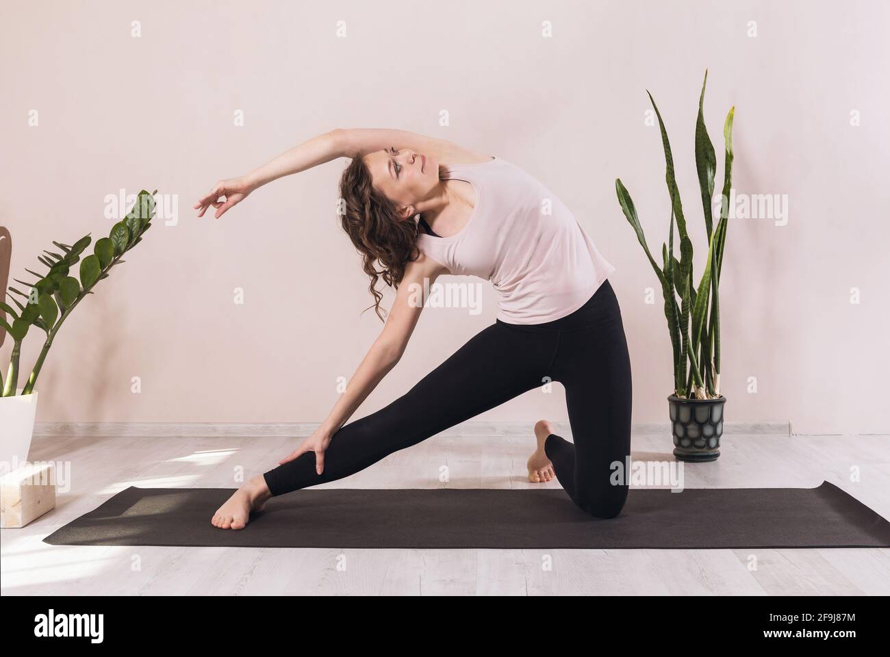 Femme pratiquant le yoga, faisant de l'exercice de paraighasana, pose d'obturateur, pratiquant en studio contre le mur sur le tapis. Banque D'Images