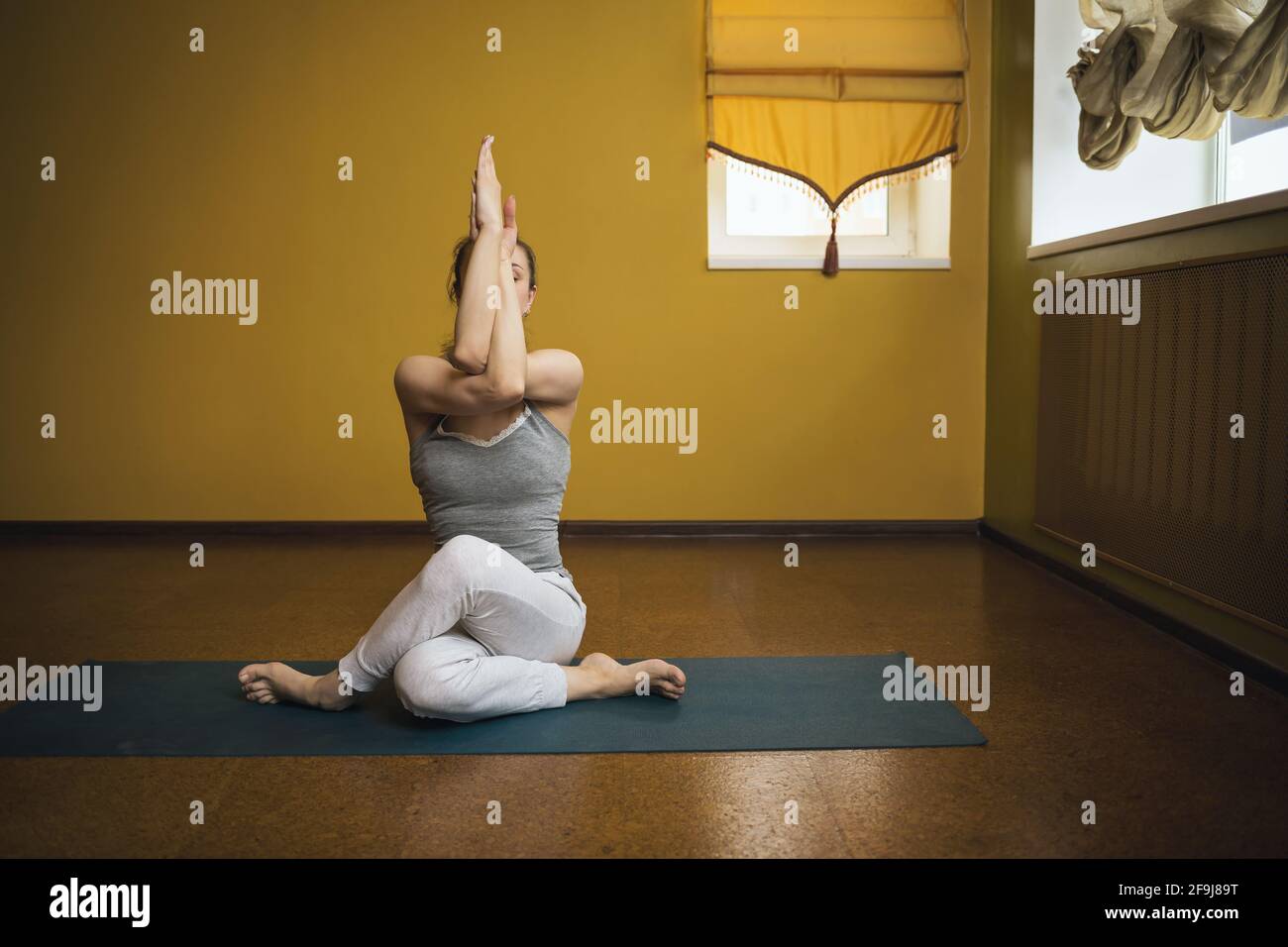 Femme en gris sportswear pratiquant le yoga, exécutant l'exercice gomukhasana, pose de vache, s'exerçant assis sur le tapis dans le studio. Banque D'Images