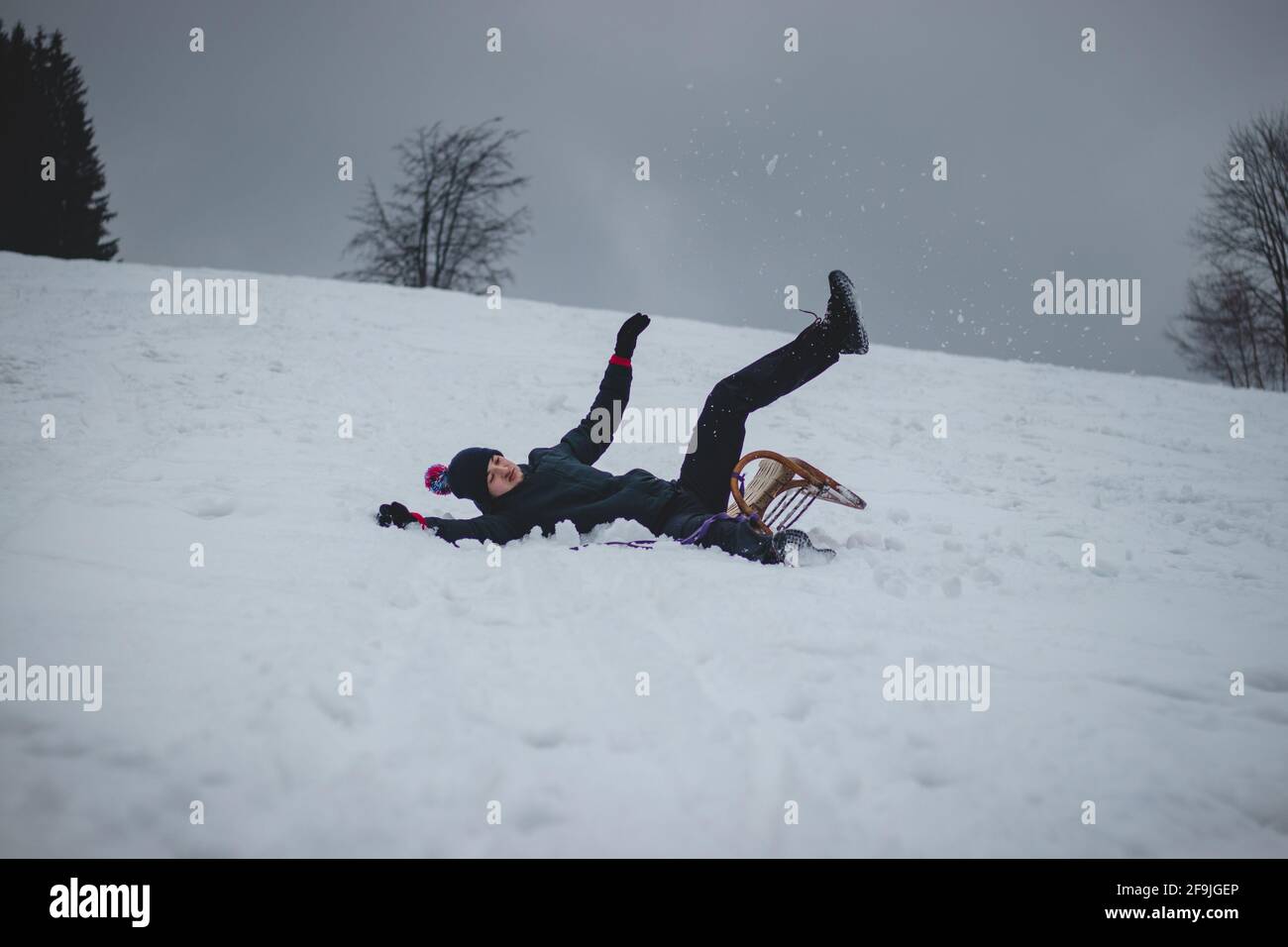 L'athlète tombe d'un traîneau en bois et tombe dur sur la neige et les entorses. Le traîneau du garçon s'est coincé et il l'a jeté et il a fait un somersault. Dur Banque D'Images