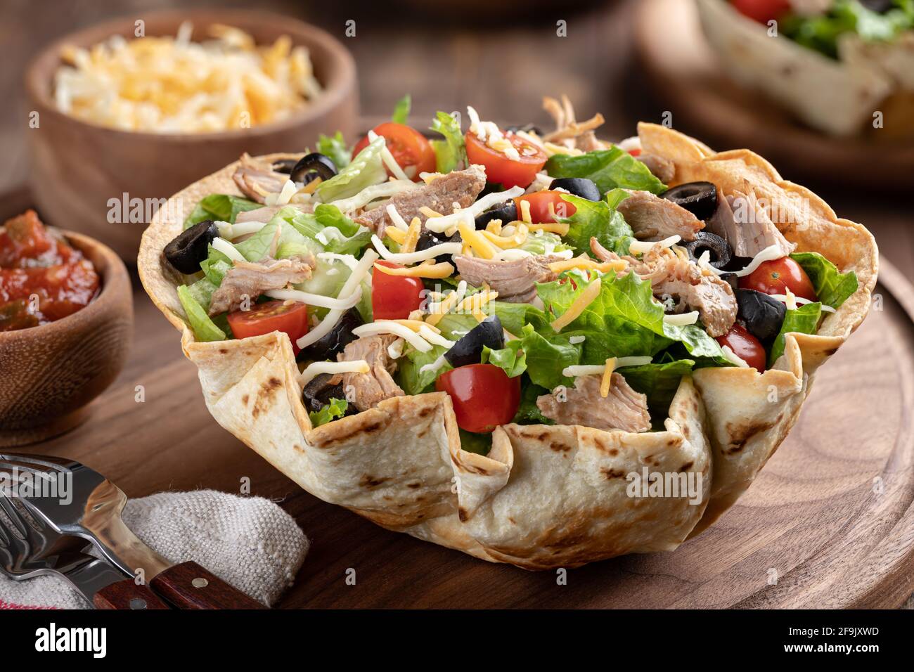 Gros plan d'une salade de tacos avec tomate, laitue, olives noires, fromage et porc dans une carapace de tortilla sur une planche en bois Banque D'Images