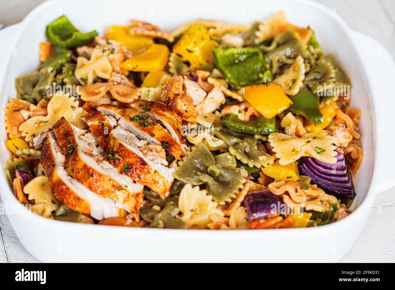 Pâtes Farfalle avec légumes cuits au four et poulet dans un plat blanc, fond gris. Banque D'Images