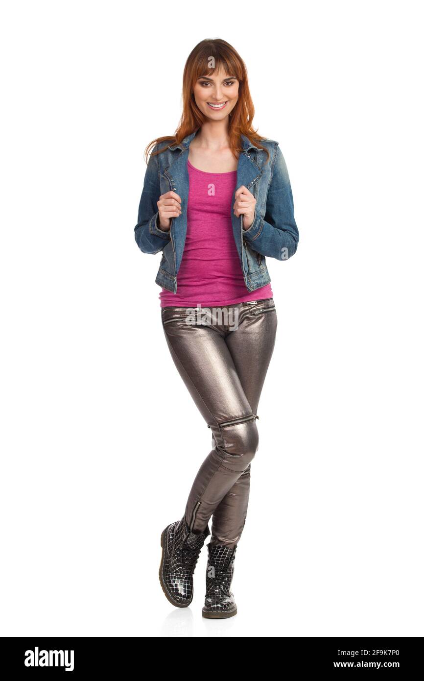 Une jeune femme souriante pose dans une veste de Jean, un pantalon brillant et des baskets. Vue avant. Prise de vue en studio sur toute la longueur isolée sur blanc. Banque D'Images
