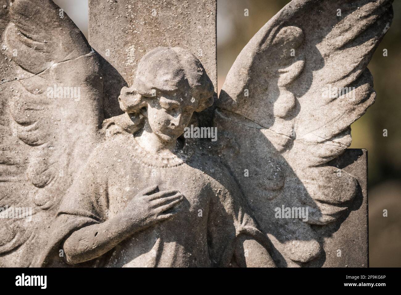 Ancienne statue de tombe en pierre d'un ange pleurant en granit avec aile cassée tenant la poitrine. Triste paisible au soleil doré. Banque D'Images