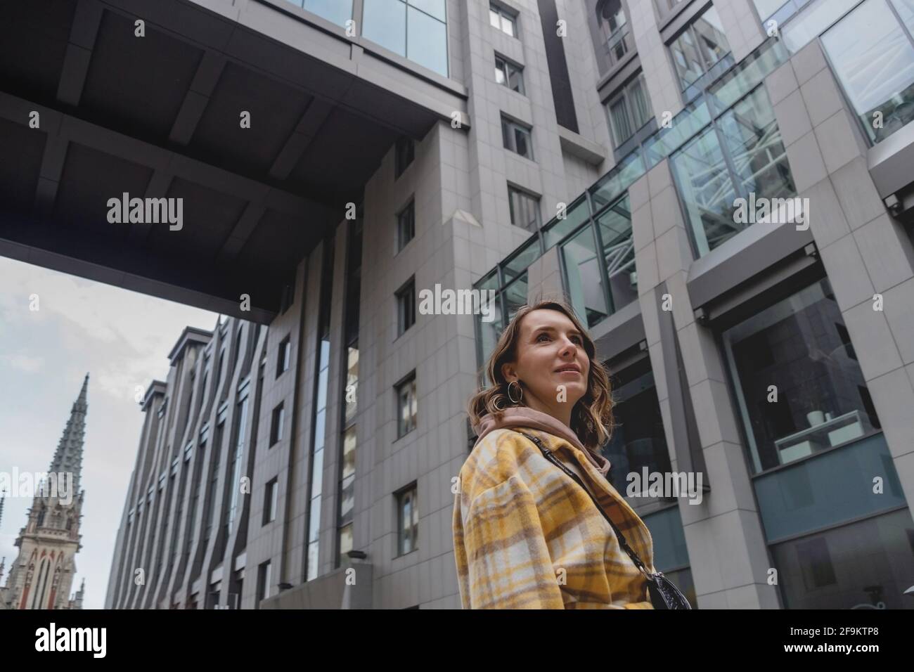 Une femme d'affaires heureuse, sous un manteau jaune, va dans un centre d'affaires d'une grande ville. Banque D'Images