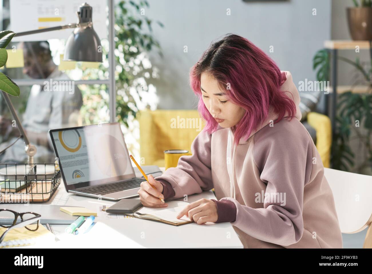 Jeune chinoise assise à la table et écrivant elle faire son travail pendant l'étude Banque D'Images