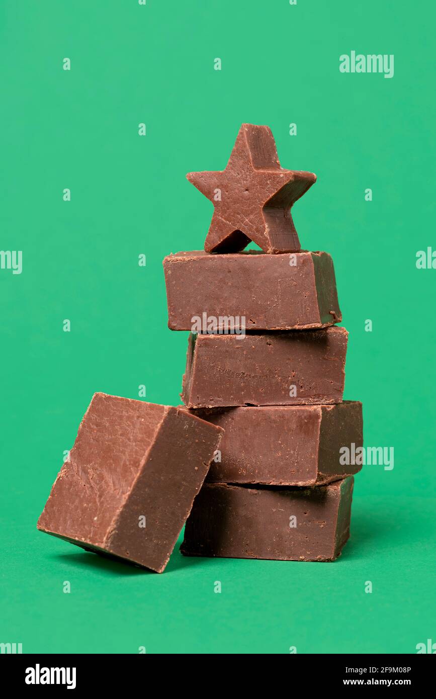 Morceaux de caramel au chocolat empilés sur une table verte. Tranches de fudge maison dans une pile isolée sur un fond coloré. Banque D'Images