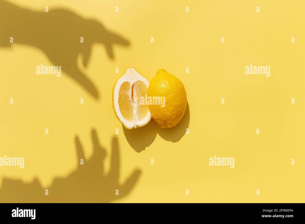 Deux demi-morceaux de citron avec ombre de la main sur fond jaune. Concept de saine alimentation, de voyage ou de vacances Banque D'Images