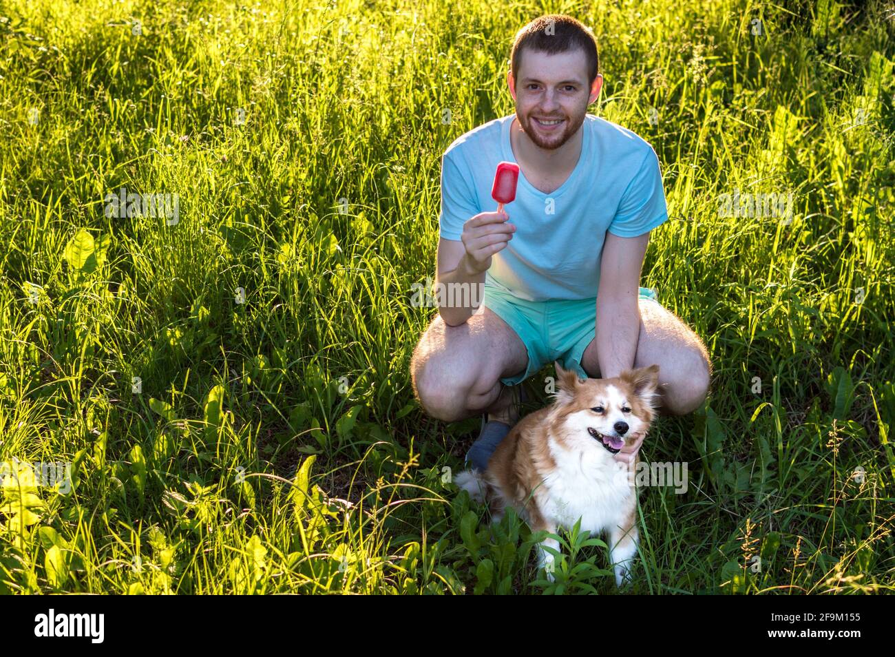 jeune homme mangeant de la glace tout en étant assis dans l'herbe avec son chien. Concept d'été. Banque D'Images