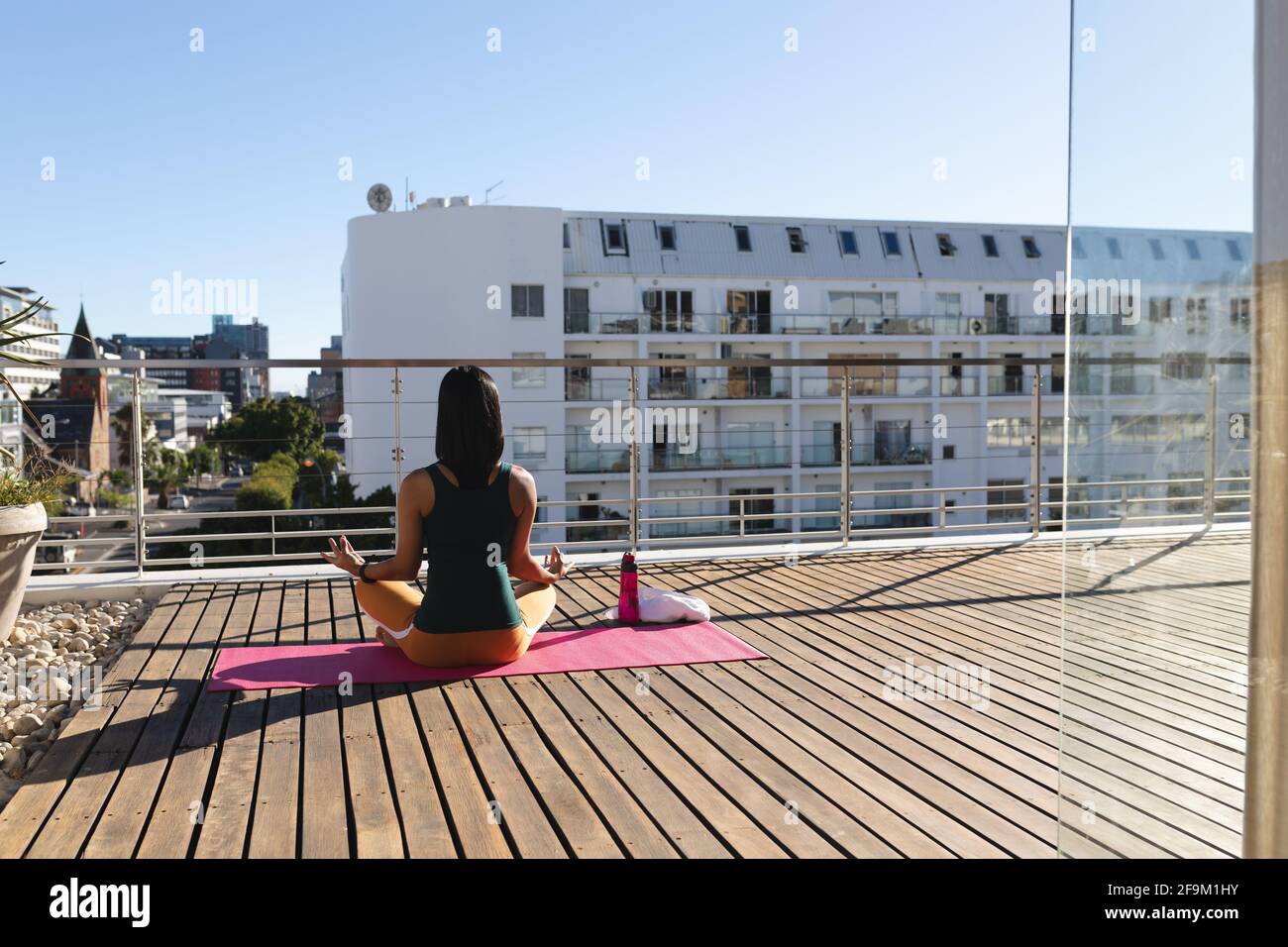 Vue arrière de la femme transgenre de race mixte pratiquant la méditation de yoga sur la terrasse du toit au soleil Banque D'Images