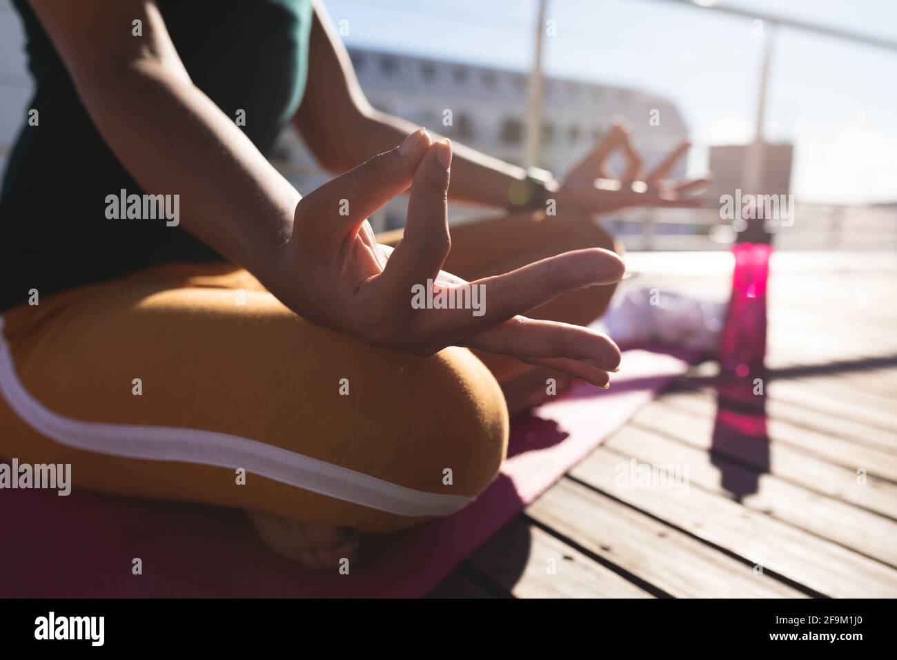 Mi-section de la race mixte transgenre femme pratiquant la méditation de yoga sur terrasse sur le toit au soleil Banque D'Images