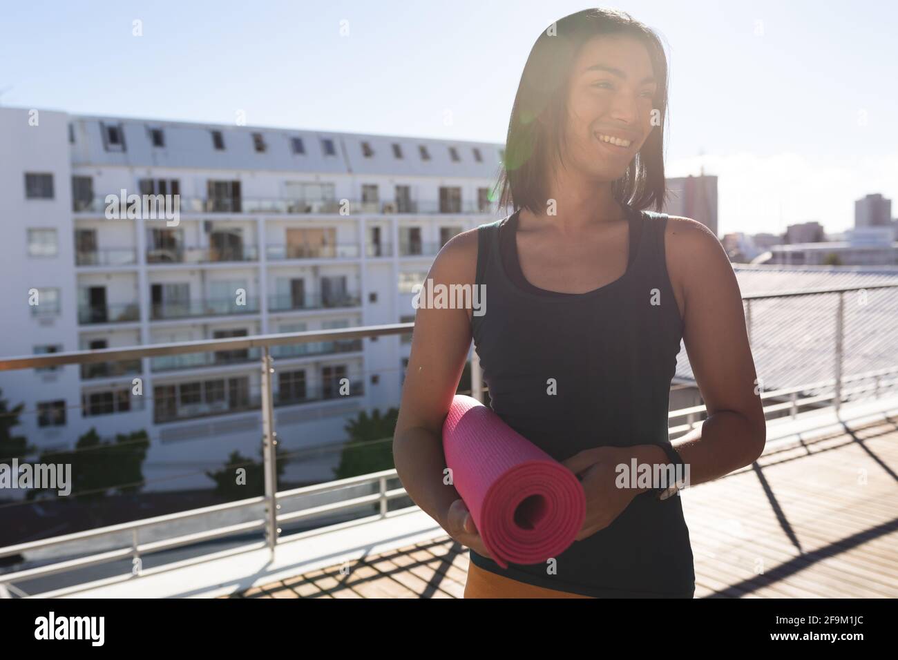 Femme transgenre de course mixte pratiquant le yoga souriant sur la terrasse du toit dans le tapis pare-soleil Banque D'Images