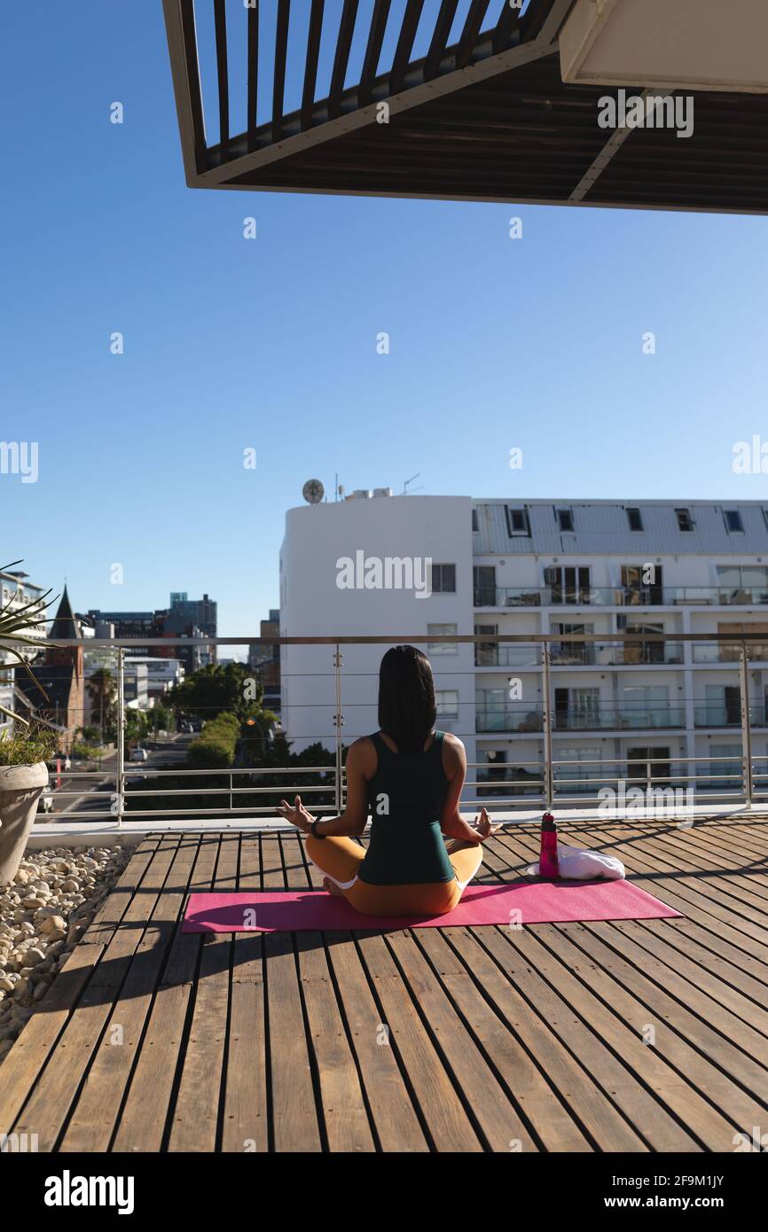 Vue arrière de la femme transgenre de race mixte pratiquant la méditation de yoga sur la terrasse du toit au soleil Banque D'Images