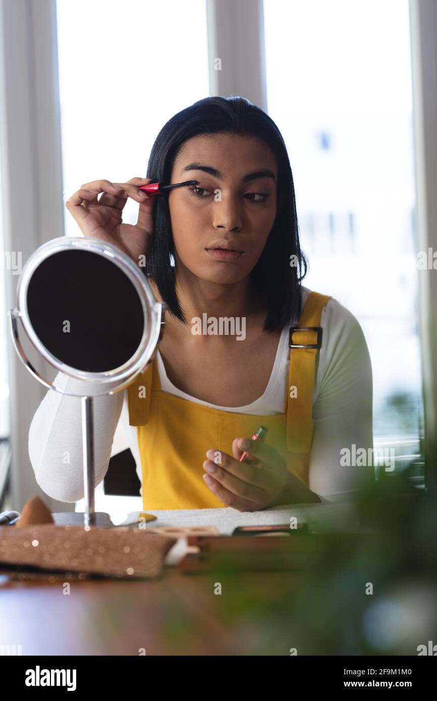 Femme transgenre de race mixte assise à une table regardant dans le miroir mettre du mascara Banque D'Images