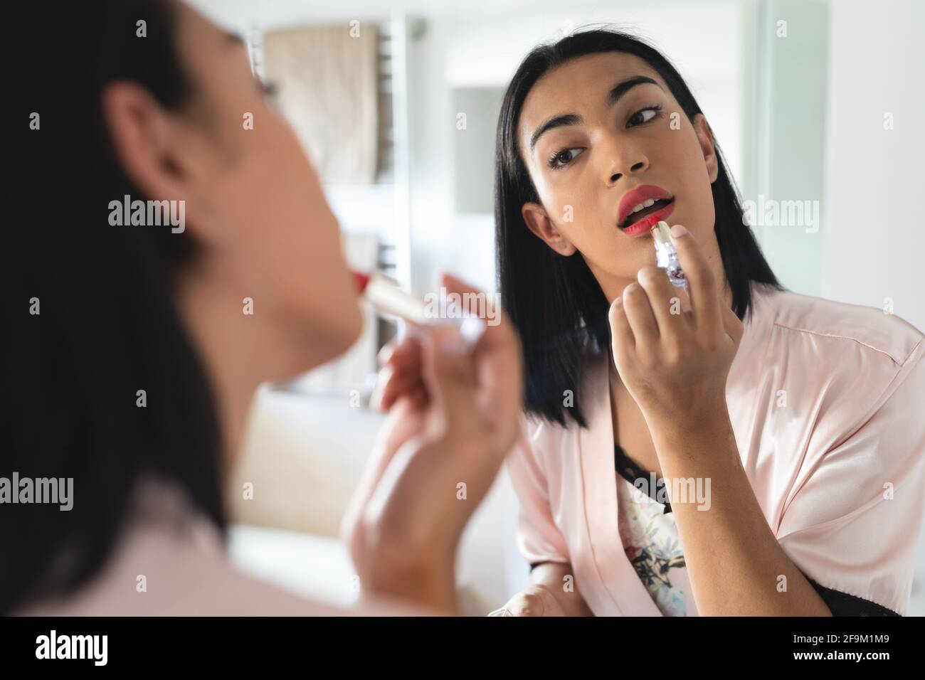 Femme transgenre de race mixte regardant dans le miroir de salle de bains et de mettre sur le rouge à lèvres Banque D'Images