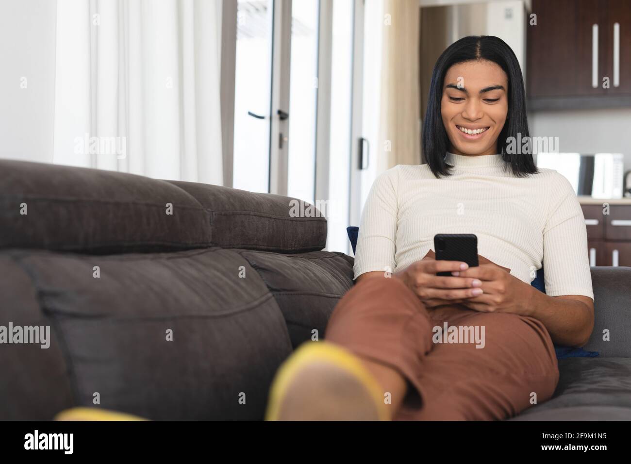Bonne femme transgenre de race mixte se détendant dans le salon assis sur le canapé prenant des selfies Banque D'Images