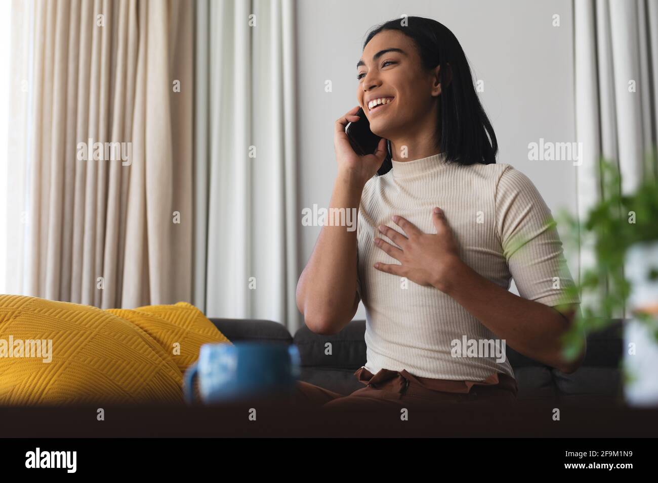 Bonne femme transgenre de race mixte se détendant dans le salon assis sur le canapé parlant au téléphone Banque D'Images