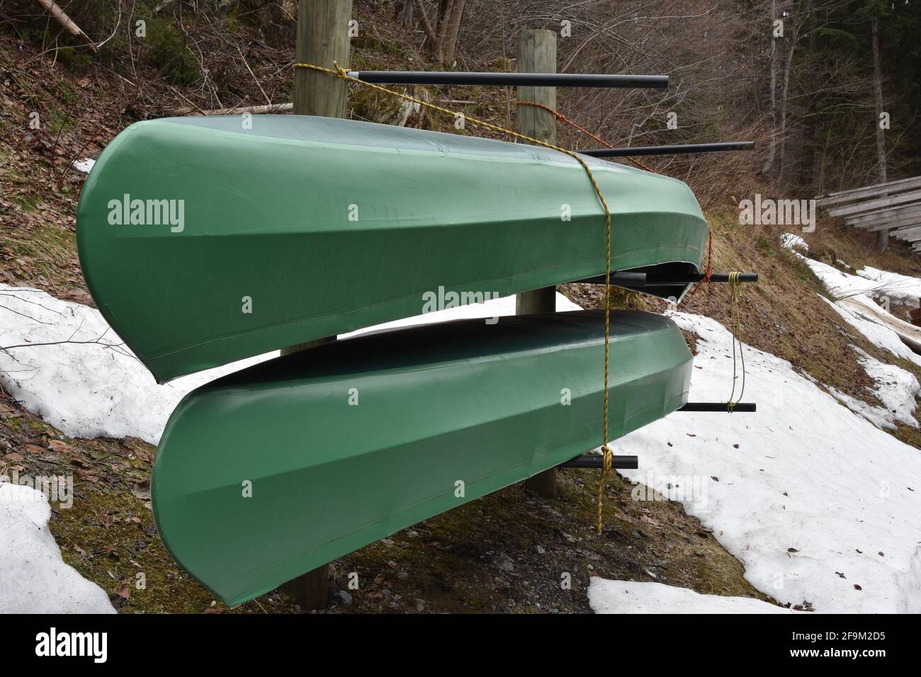 Deux kayaks verts rangés dans des casiers à l'envers dans la vue latérale. Ils attendent le début de la saison des sports nautiques. Il y a des taches de neige autour d'eux. Banque D'Images