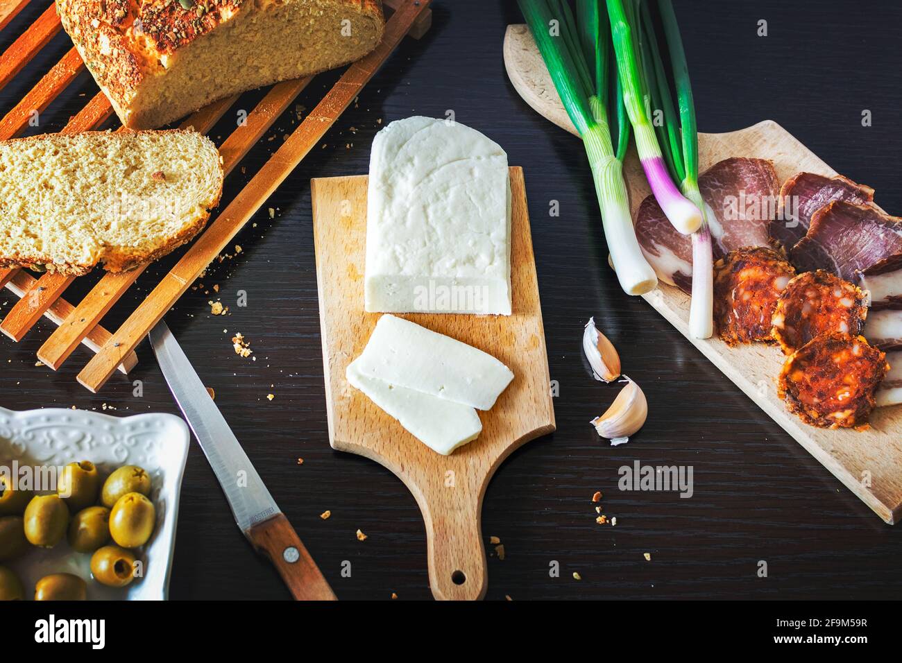 Fromage Haloumi avec pain frais, oignons verts, jambon fumé et saucisses, olives sur une table à manger en bois sombre. Banque D'Images