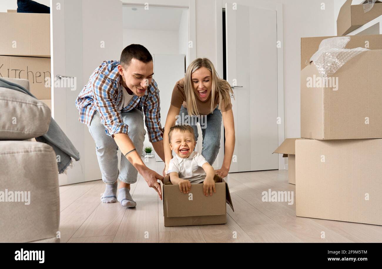 Les jeunes parents heureux poussant boîte carton avec enfant dans nouvel appartement hypothécaire. Banque D'Images