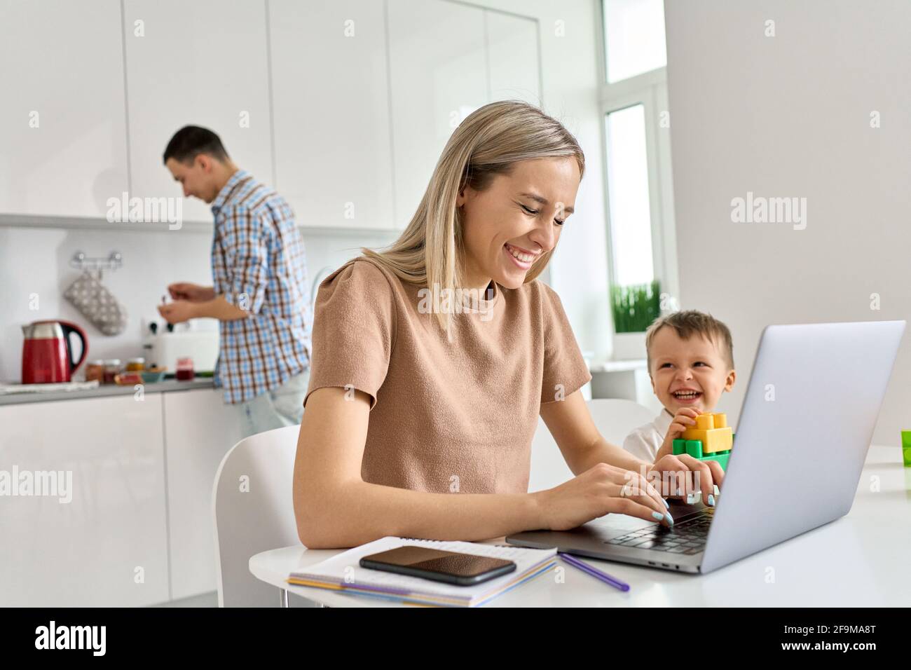 Bonne maman qui travaille à la maison en utilisant un ordinateur portable tout en jouant un drôle de fils de gamin. Banque D'Images