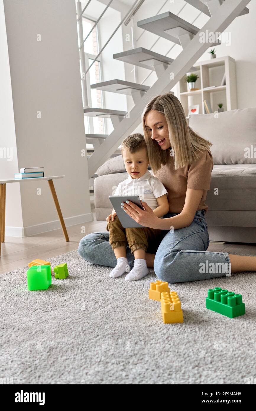 Maman souriante enseignant enfant enfant fils à l'aide d'une tablette numérique à la maison. Banque D'Images
