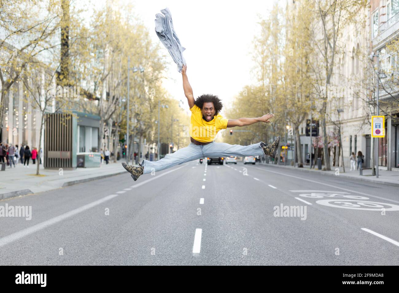 Un jeune homme noir sautant énergiquement au milieu de la rue dans une grande ville. Il a une coiffure afro et des robes à la mode. Espace pour le texte. Banque D'Images