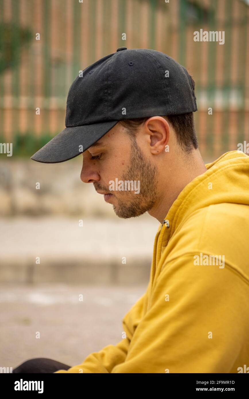 Portrait d'un jeune homme portant un pull à capuche jaune et chapeau noir dans une rue Banque D'Images