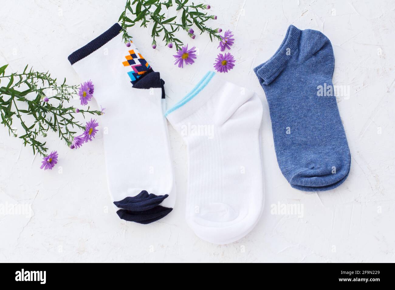 Trois paires de chaussettes et de fleurs pour femmes sur fond blanc structuré, vue du dessus. Banque D'Images