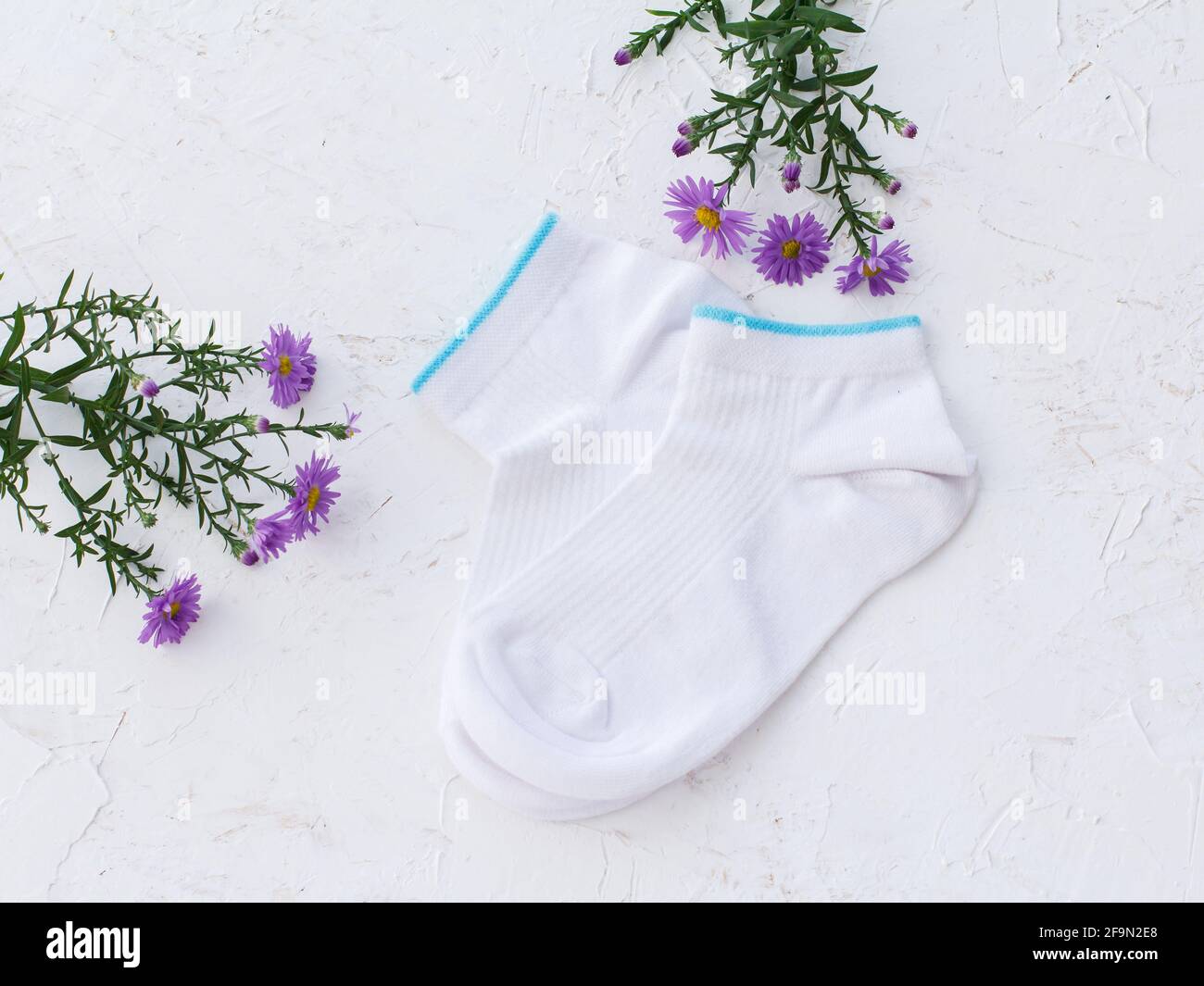 Deux paires de chaussettes et de fleurs pour femmes sur fond blanc structuré, vue du dessus. Banque D'Images