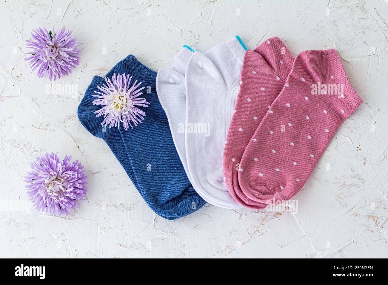 Trois paires de chaussettes bleues, blanches et roses pour femmes avec boutons de fleurs d'aster sur fond blanc structuré, vue du dessus. Banque D'Images