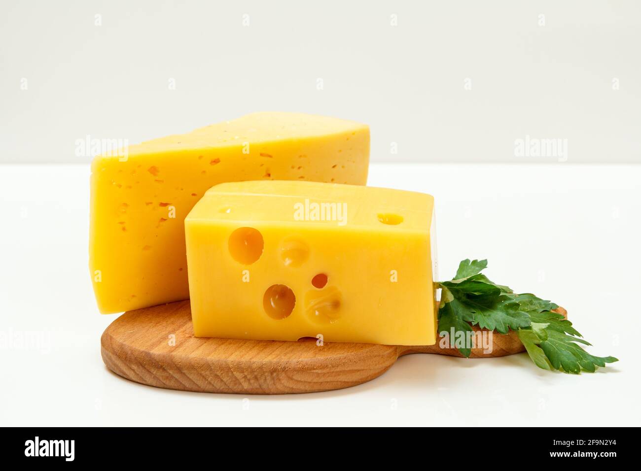 Fromage et persil sur planche à découper en bois sur fond blanc Banque D'Images