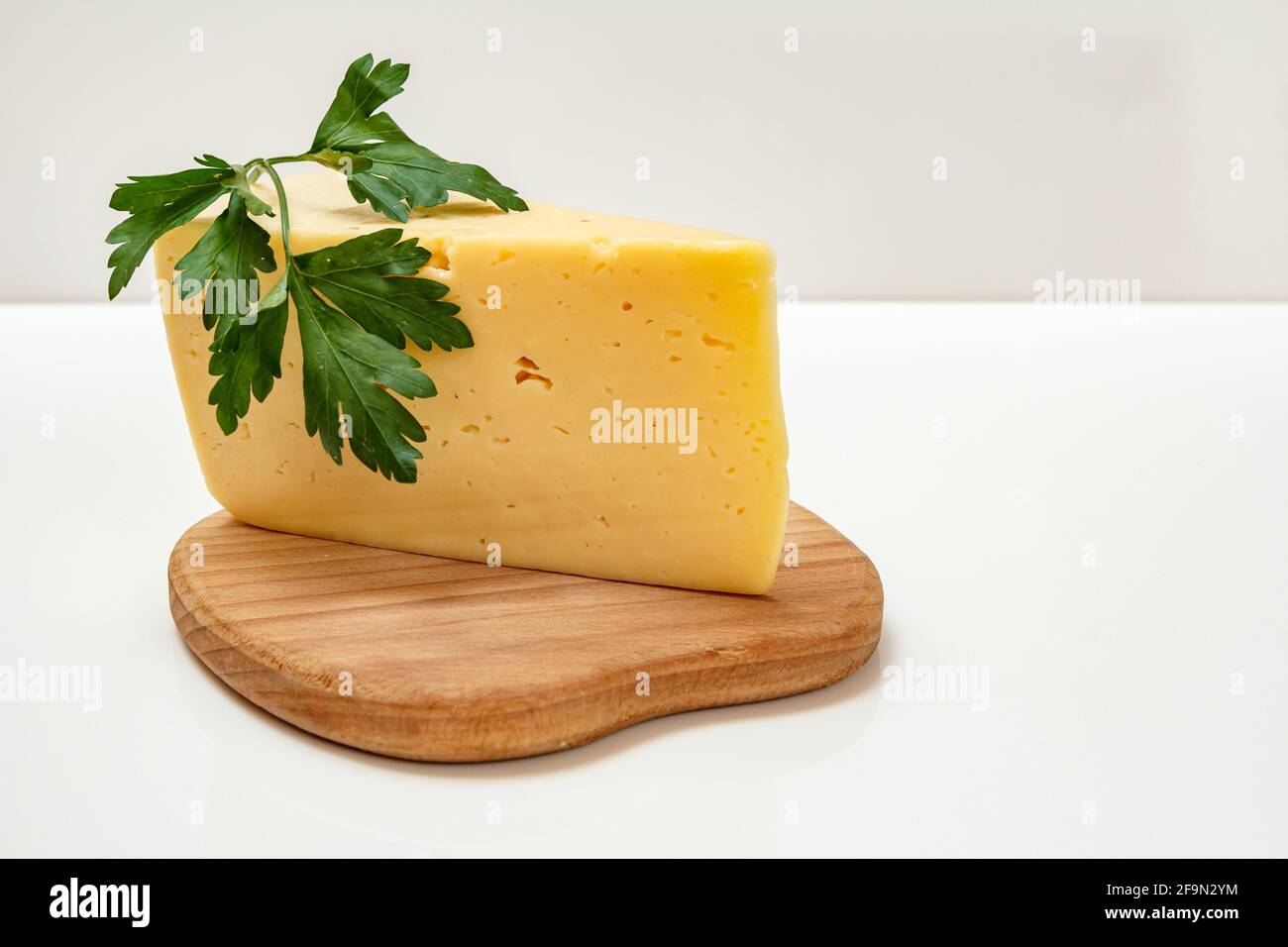 Fromage et persil sur planche à découper en bois sur fond blanc Banque D'Images