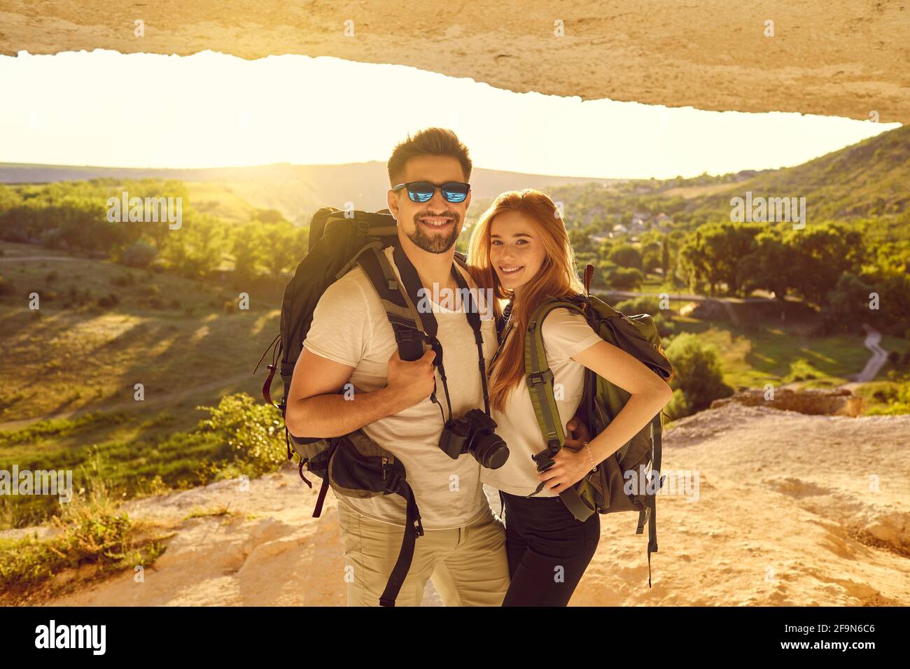 Joyeux jeune couple de randonneurs debout dans la grotte des montagnes au coucher du soleil. Touristes alpinisme en vacances d'été Banque D'Images