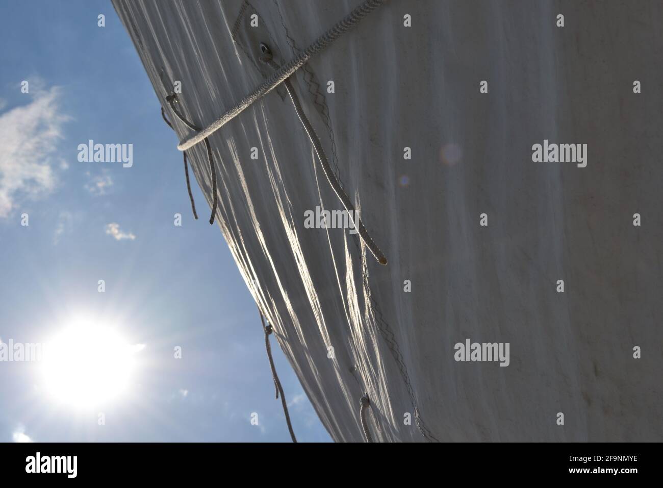 Un soleil spectaculaire se délayant sur la voile blanche d'un bateau ; un soleil éclatant brille dans un ciel bleu, au-dessus de la voile et des points de récif de corde Banque D'Images