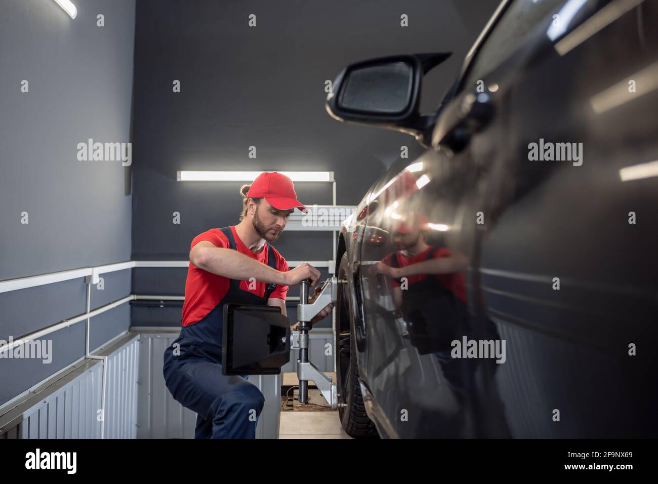 Travailleur dans une combinaison près de la roue de la voiture Banque D'Images